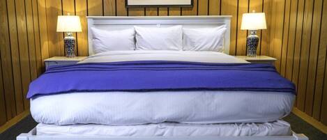 A neatly made bed with white and blue bedding, two bedside lamps, and a framed picture on the wall.