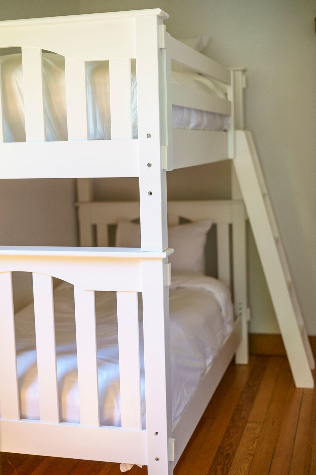 A bunk bed with a ladder, white bedding, and a wooden floor.