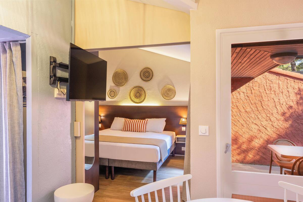 Ein Schlafzimmer mit Bett, Nachttischen, einem Fernseher und Blick ins Freie.