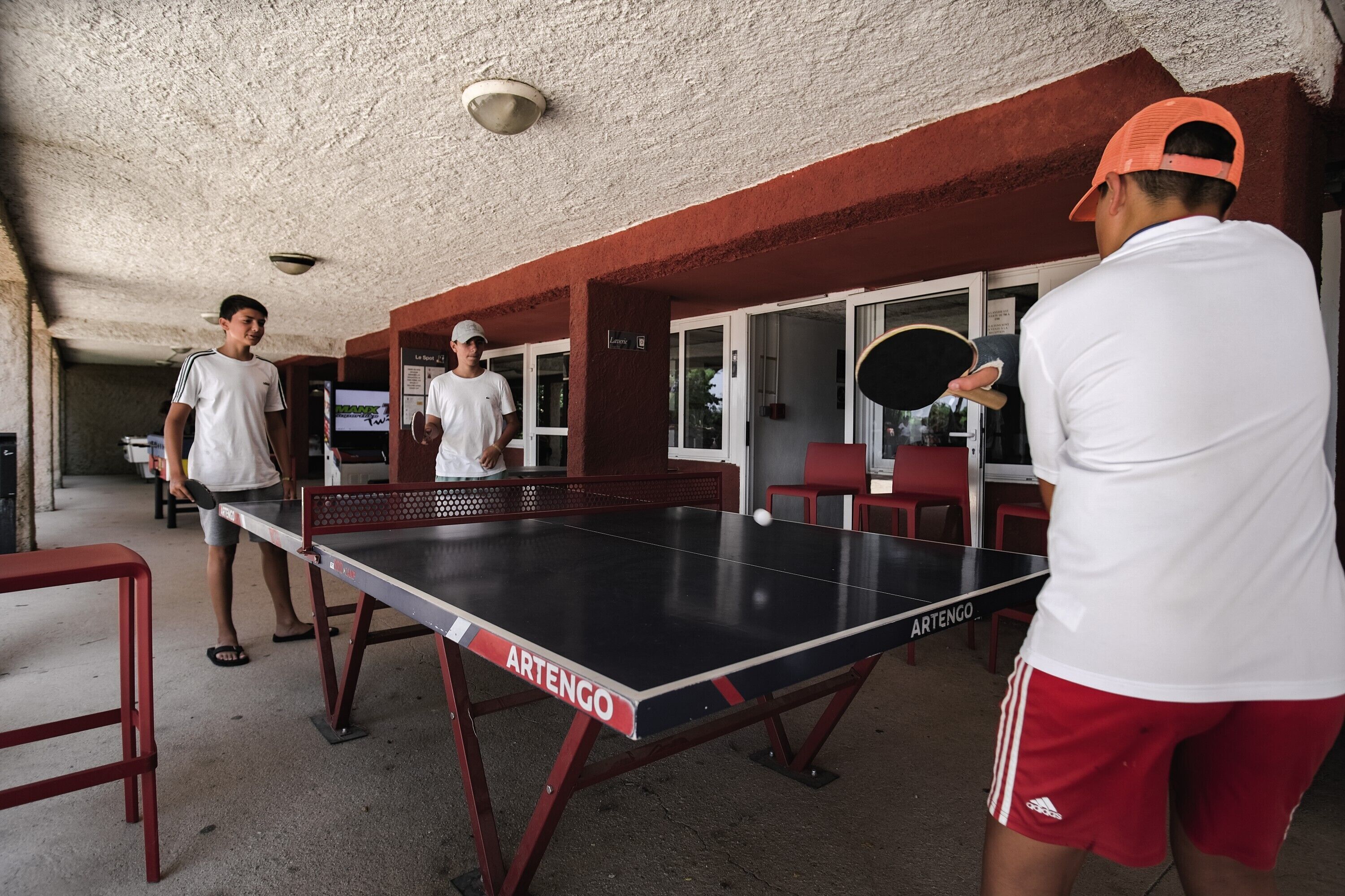 A ping pong table with two players and a third person standing nearby.