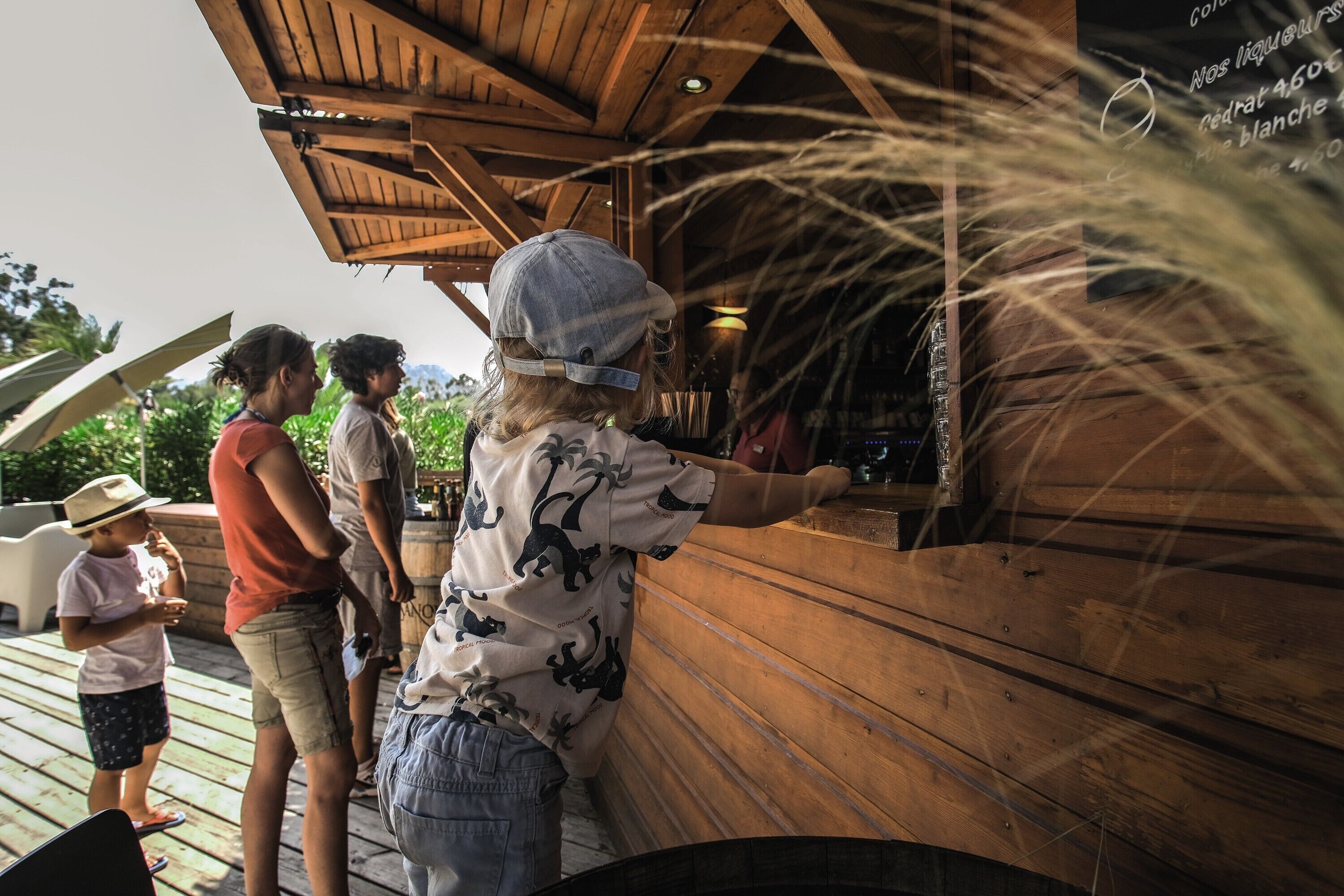 A wooden deck with a rustic wooden structure, possibly a bar or seating area, with people standing around.