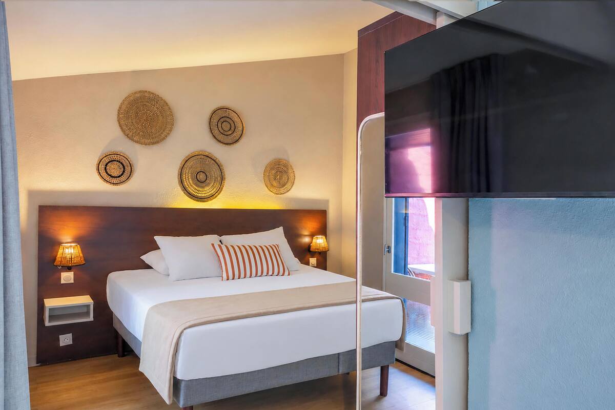 Ein Hotelzimmer mit einem Bett, Nachttischlampen, dekorativen Wandschildern und einem Fenster mit Vorhängen.