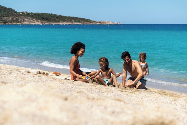 A beach scene with people sitting on the sand, a clear blue sky, and calm sea.