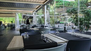 Ein Restaurant im Freien mit gedeckten Tischen, großen Fenstern und Blick auf Grünflächen.