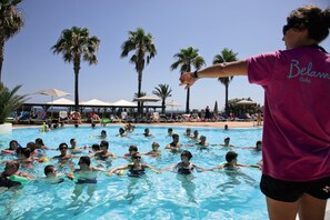 Una piscina con gente nadando, palmeras y sombrillas de playa al fondo.