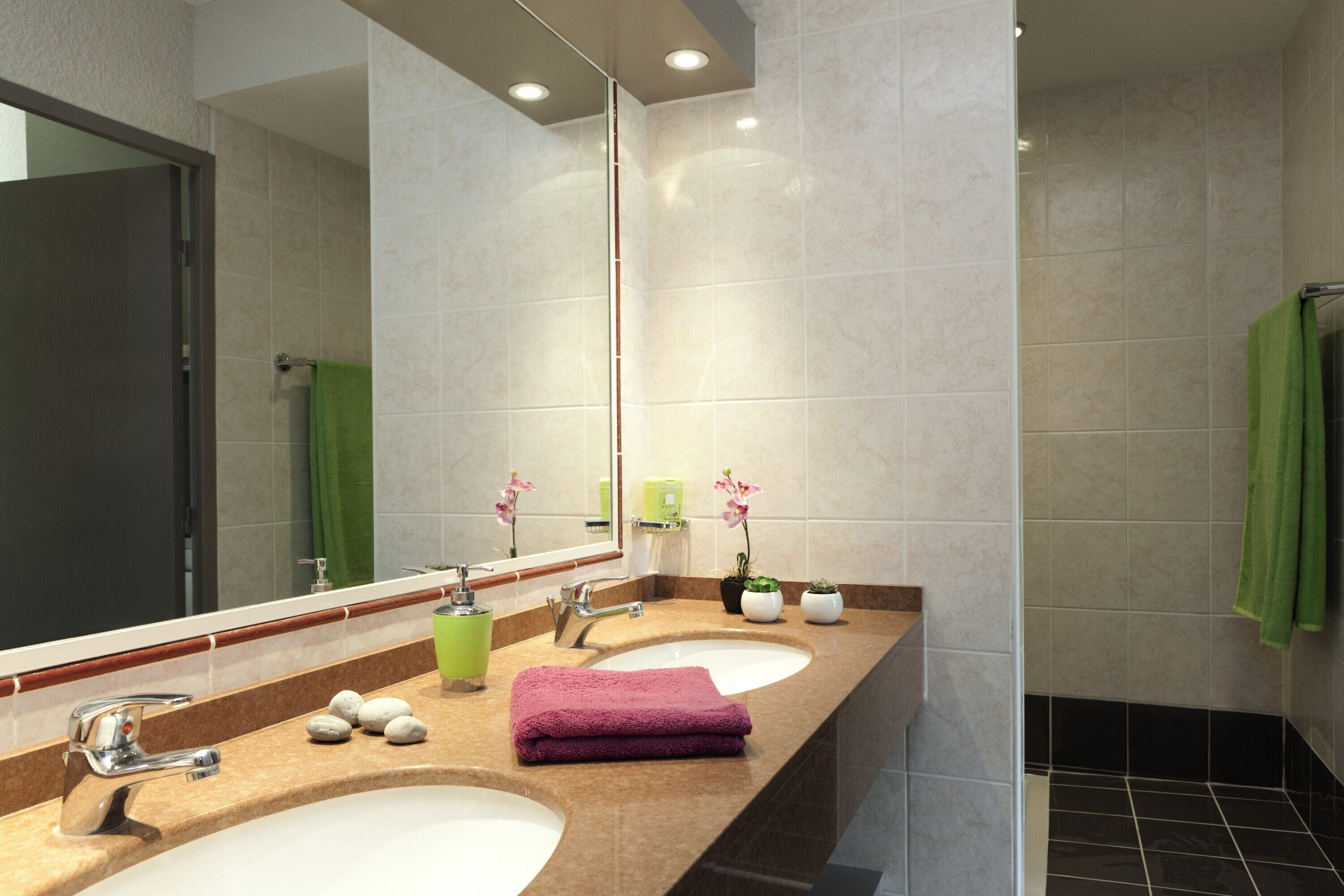 A modern bathroom with two sinks, a large mirror, and a green towel.