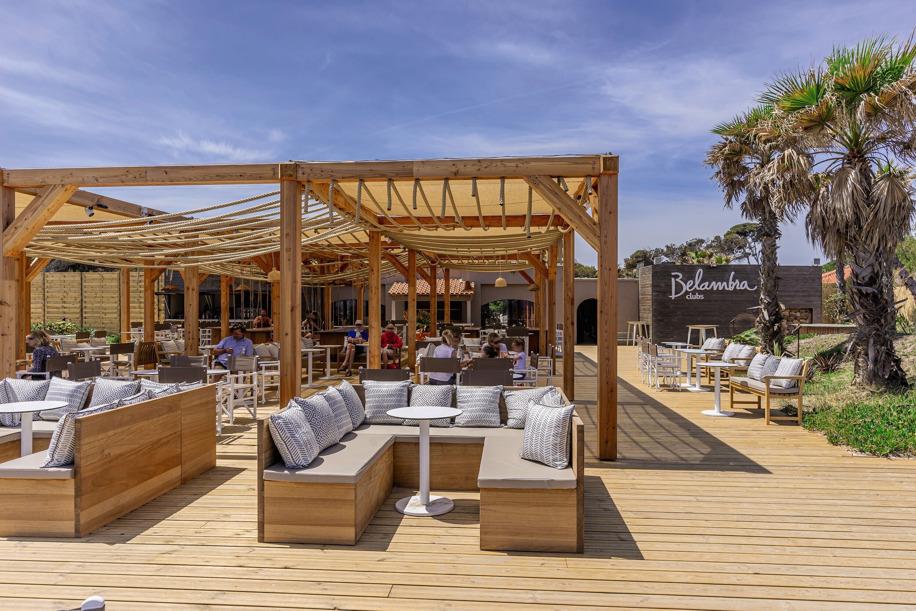 An outdoor seating area with wooden benches and tables, a pergola structure, and a sign for 'Belambra clubs'.