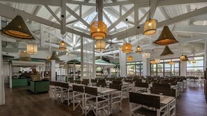 A spacious indoor dining area with high ceilings, exposed beams, and natural light from large windows. Tables are arranged in rows with chairs, and hanging wicker lamps provide lighting. - Belambra Clubs Presqu'île de Giens - Riviera Beach Club (Hyères)