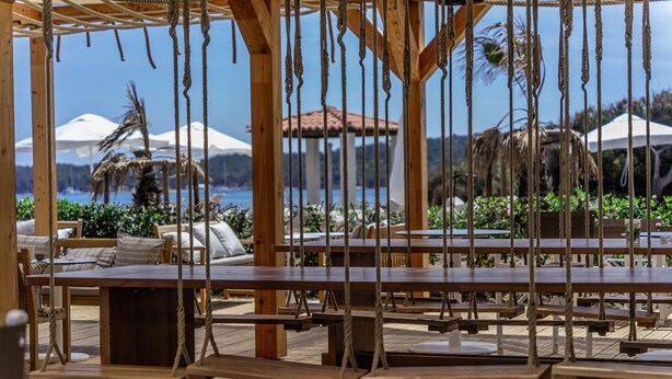 A wooden deck with benches and ropes, overlooking a beach with umbrellas and palm trees. - Belambra Clubs Presqu'île de Giens - Riviera Beach Club (Hyères)