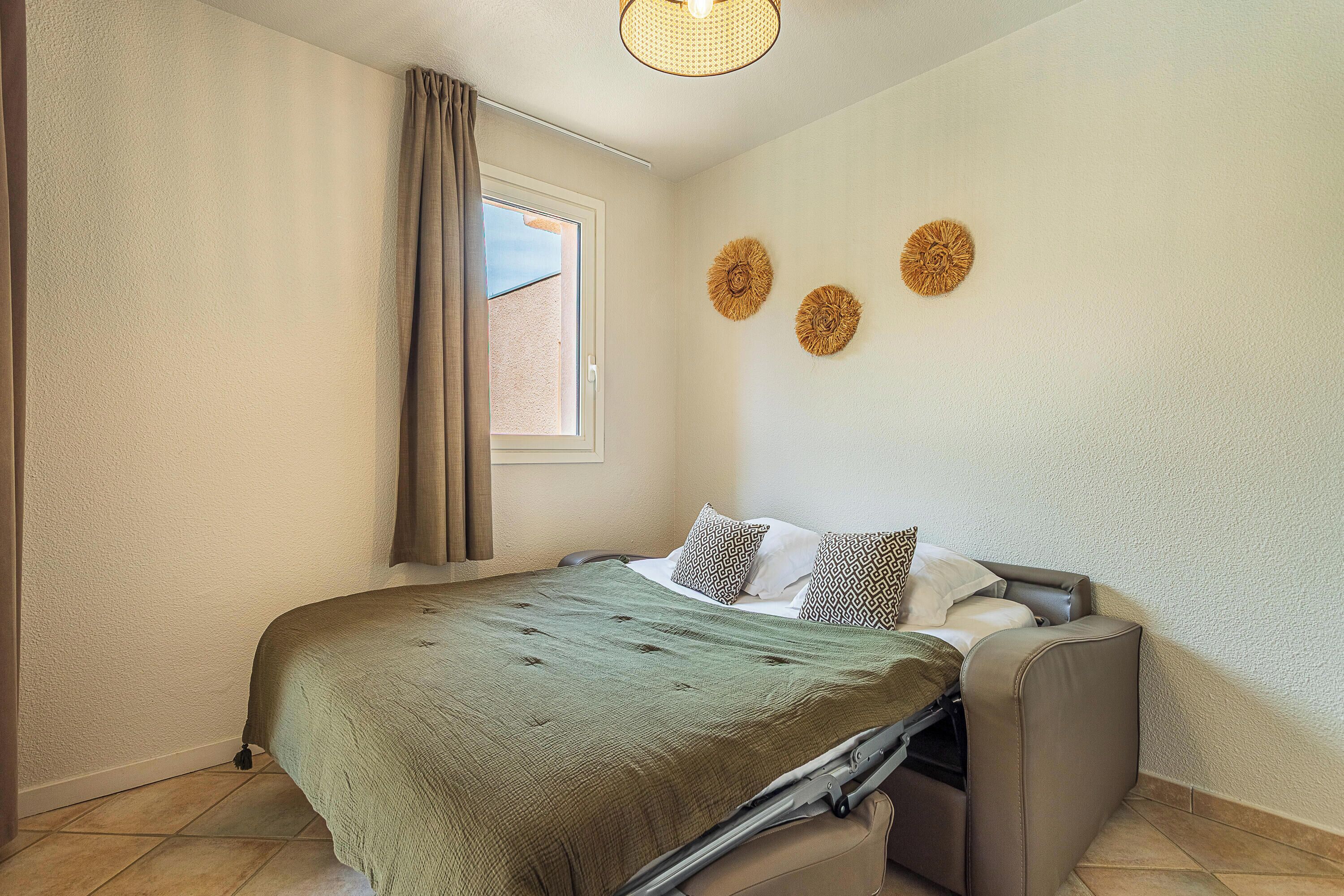 A bedroom with a bed, a window with curtains, and two wall decorations.