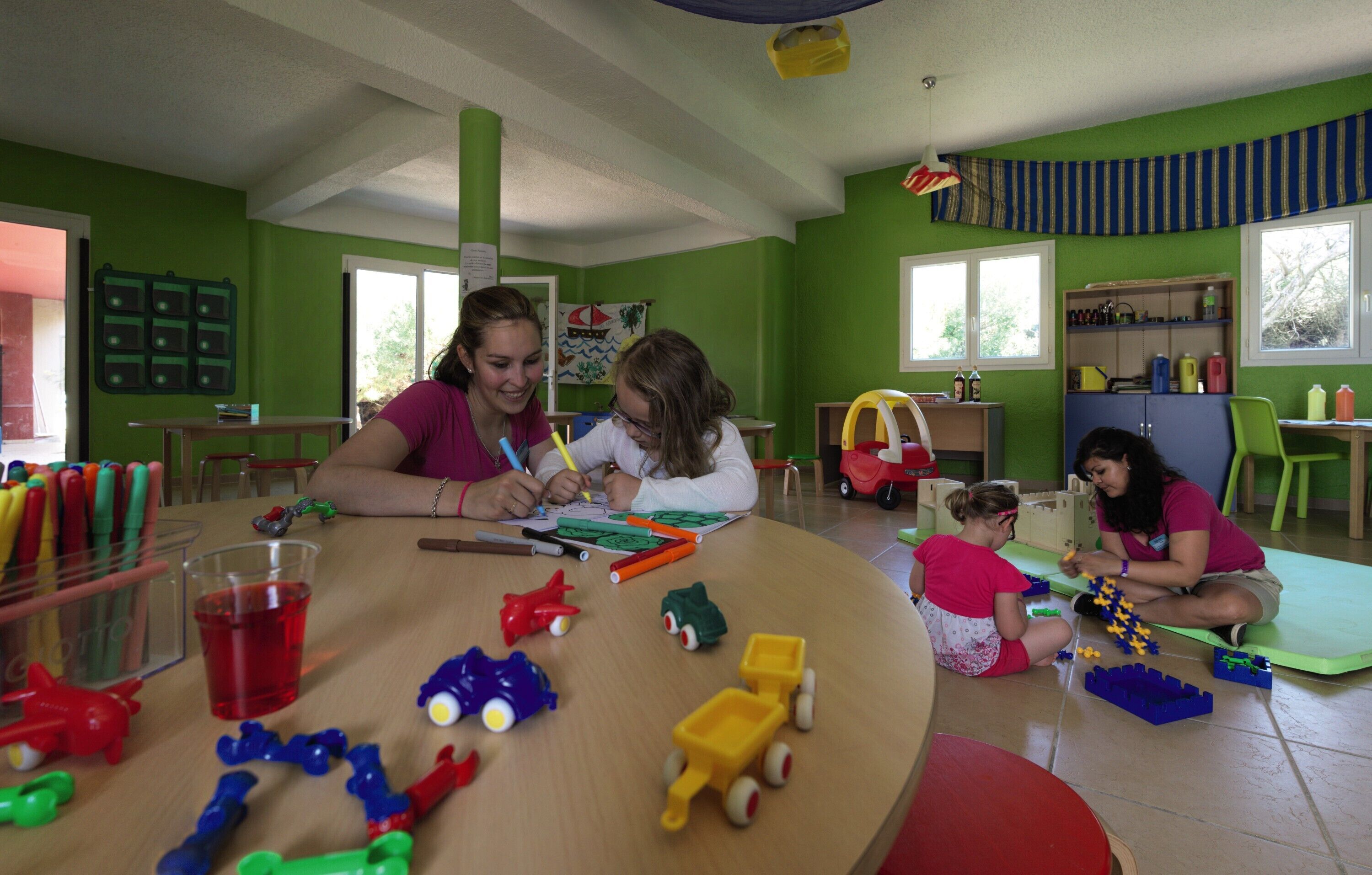 Un aula con paredes verdes, una mesa de madera y niños realizando actividades.
