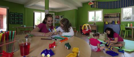 Un aula con paredes verdes, una mesa de madera y niños realizando actividades.