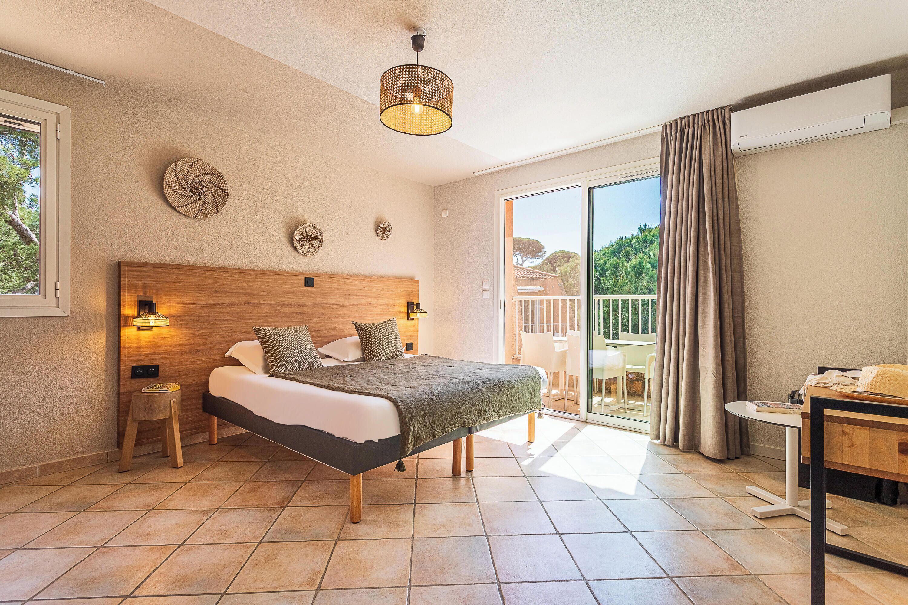 A bedroom with a bed, bedside table, lamp, and a view of the outside balcony.