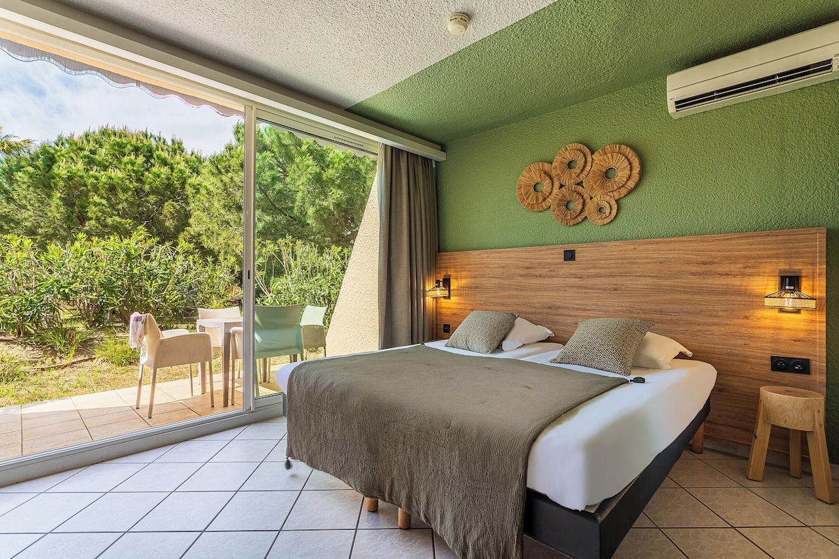 Quarto com uma cama grande, vista para o exterior e cabeceira de madeira.
