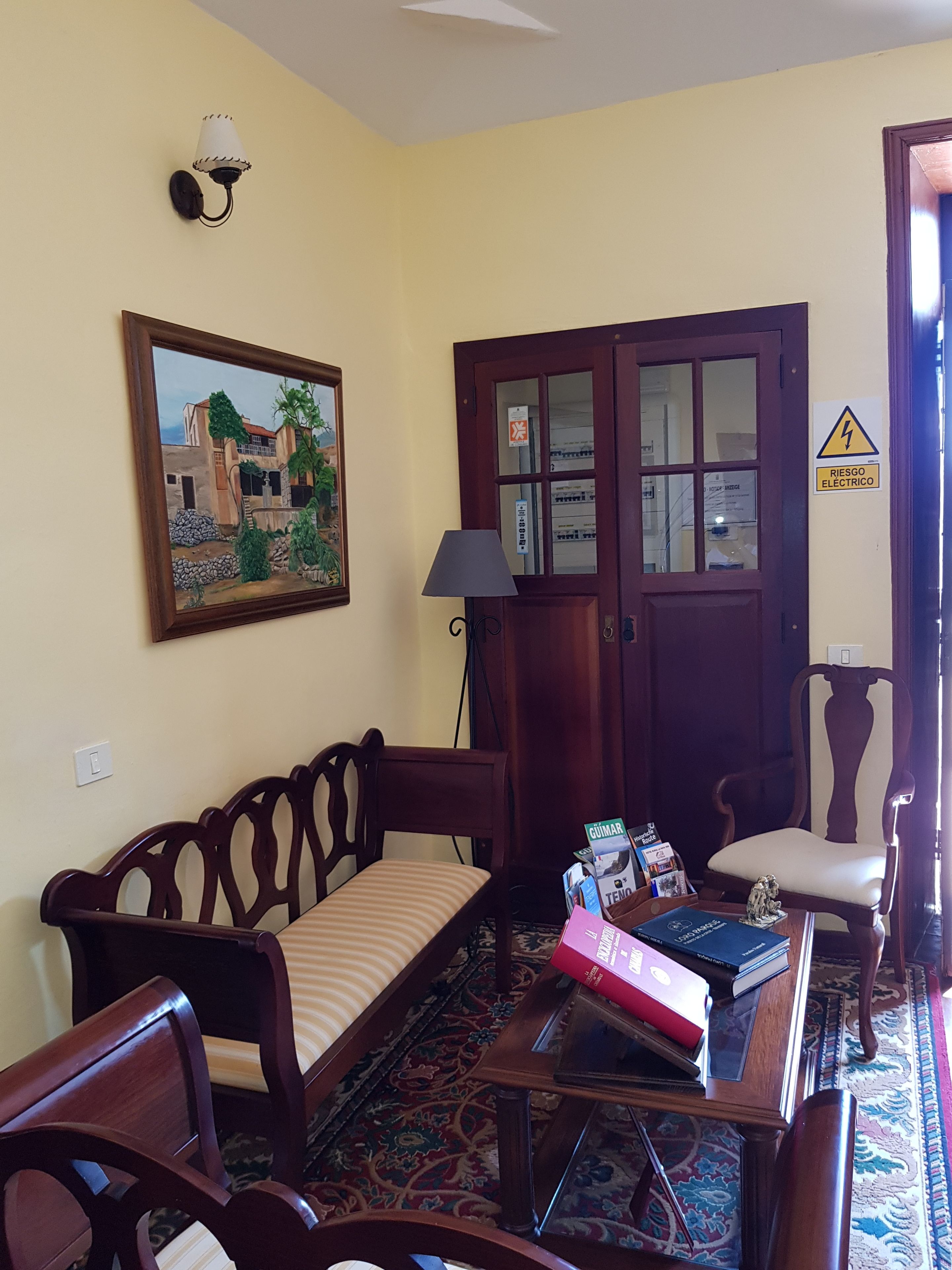 Un salón con sofá, sillas, una mesita de centro, lámpara, un cuadro y una puerta con un cartel.