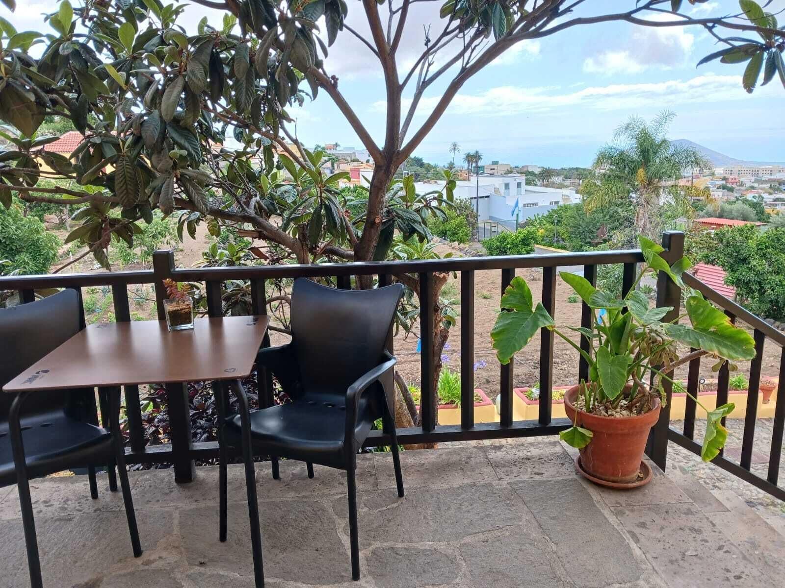 Un balcón con una mesa y sillas, una planta en maceta y vistas a edificios y una montaña en la distancia.