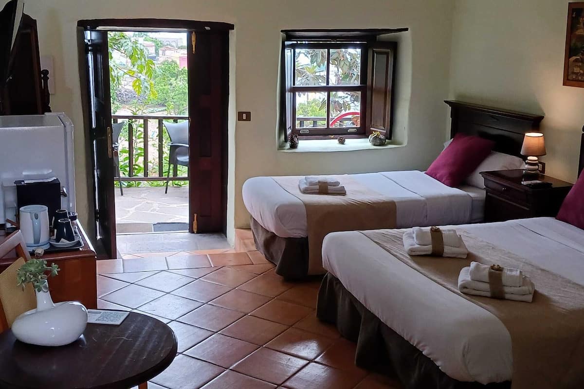 Une chambre d’hôtel avec deux lits, une petite table sur laquelle est posé un vase, une fenêtre donnant sur un espace verdoyant et une porte menant à un espace extérieur.