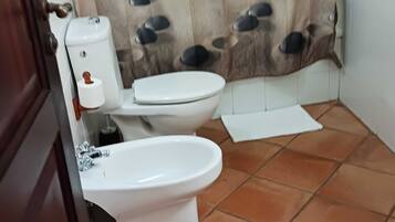 Un baño con inodoro, bidé y cortina de ducha con estampado de peces.