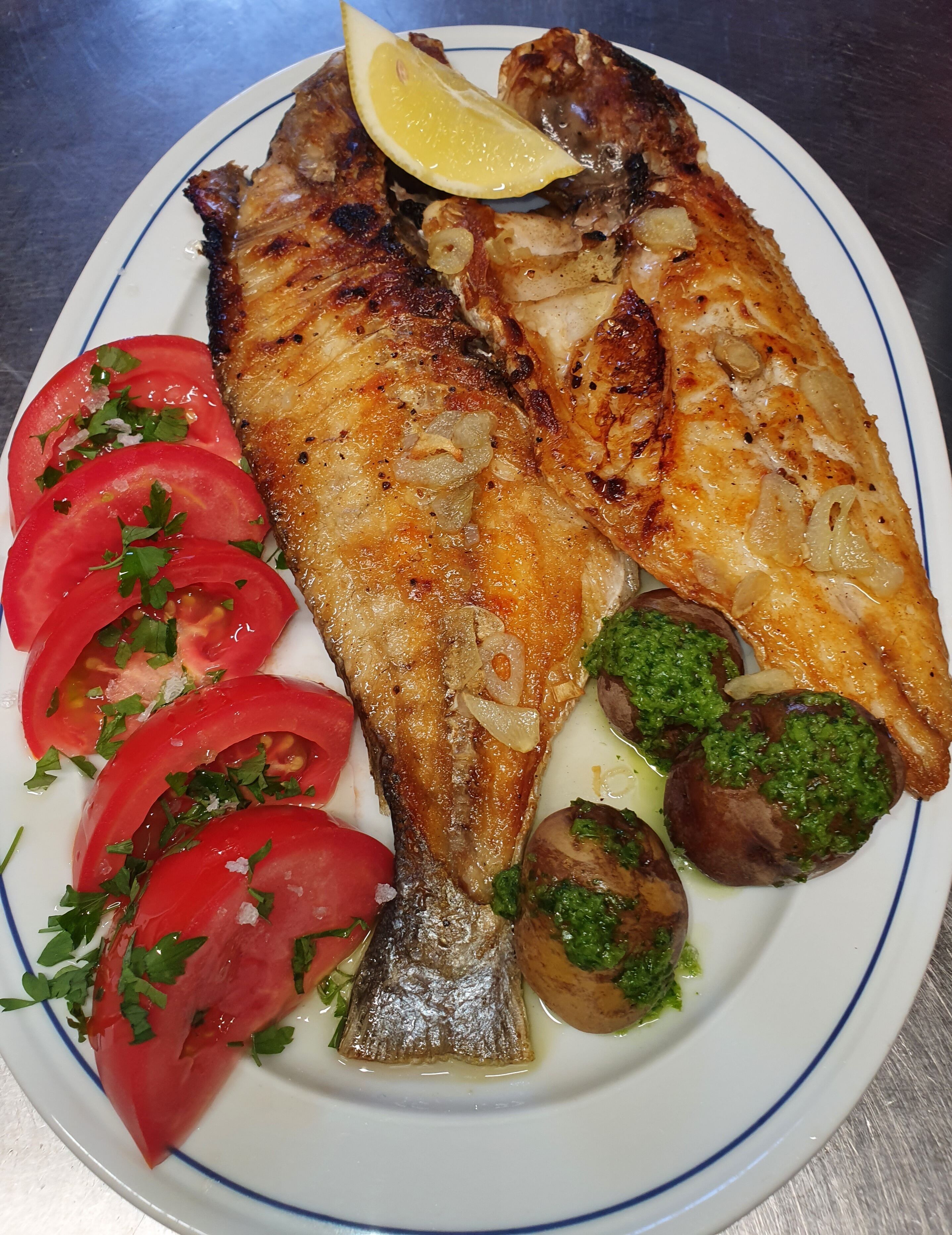 Une assiette contenant du poisson grillé, des tomates en tranches et des champignons.