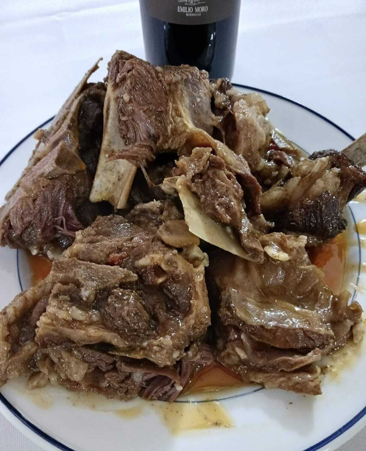 Un plato de carne cocida con huesos, posiblemente costillas, servido en un plato blanco con borde azul.