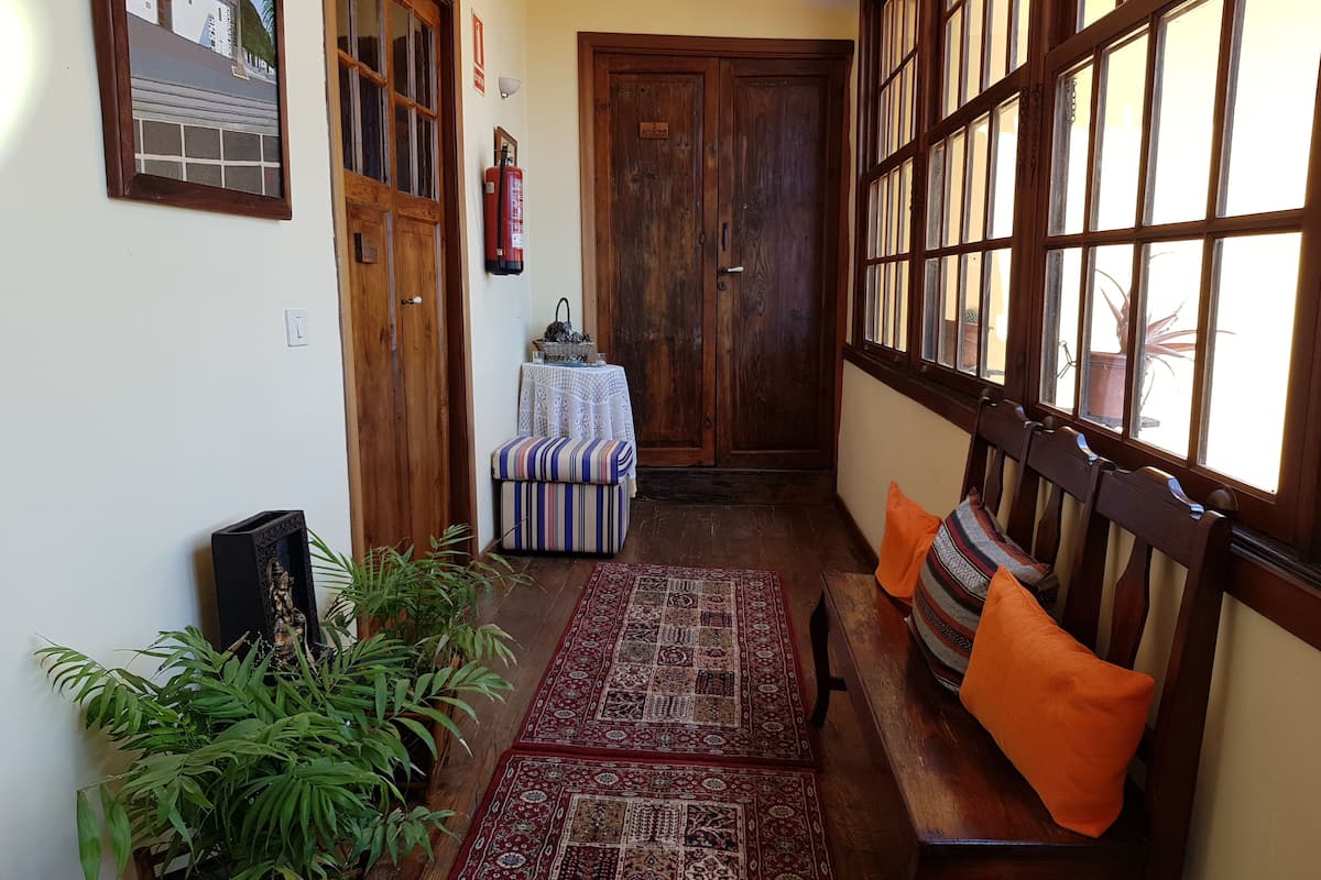 Un couloir étroit avec un banc en bois, un tapis à motifs et une table recouverte d’une nappe blanche.