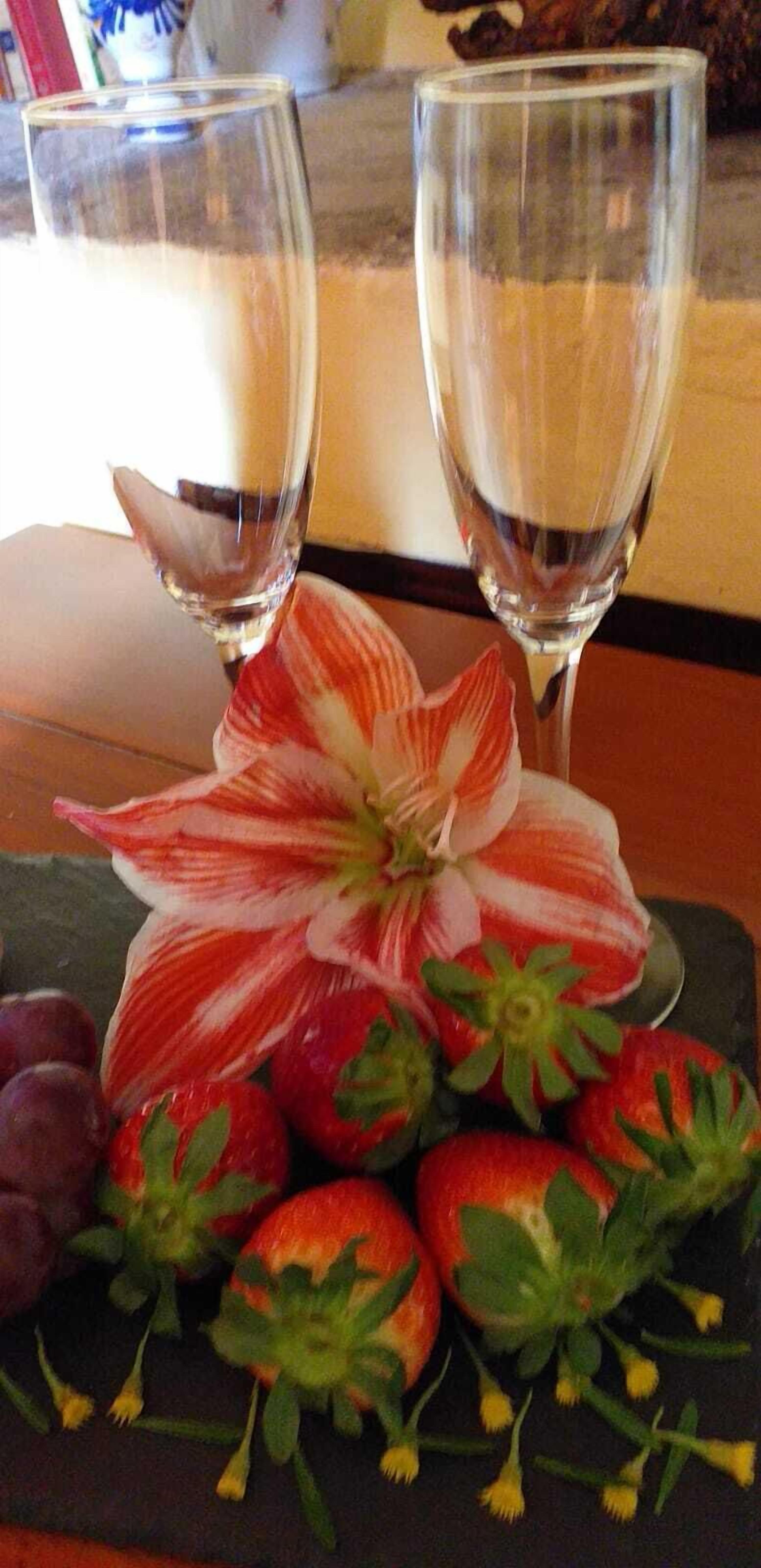 A table with two empty wine glasses and a plate of strawberries and a flower.