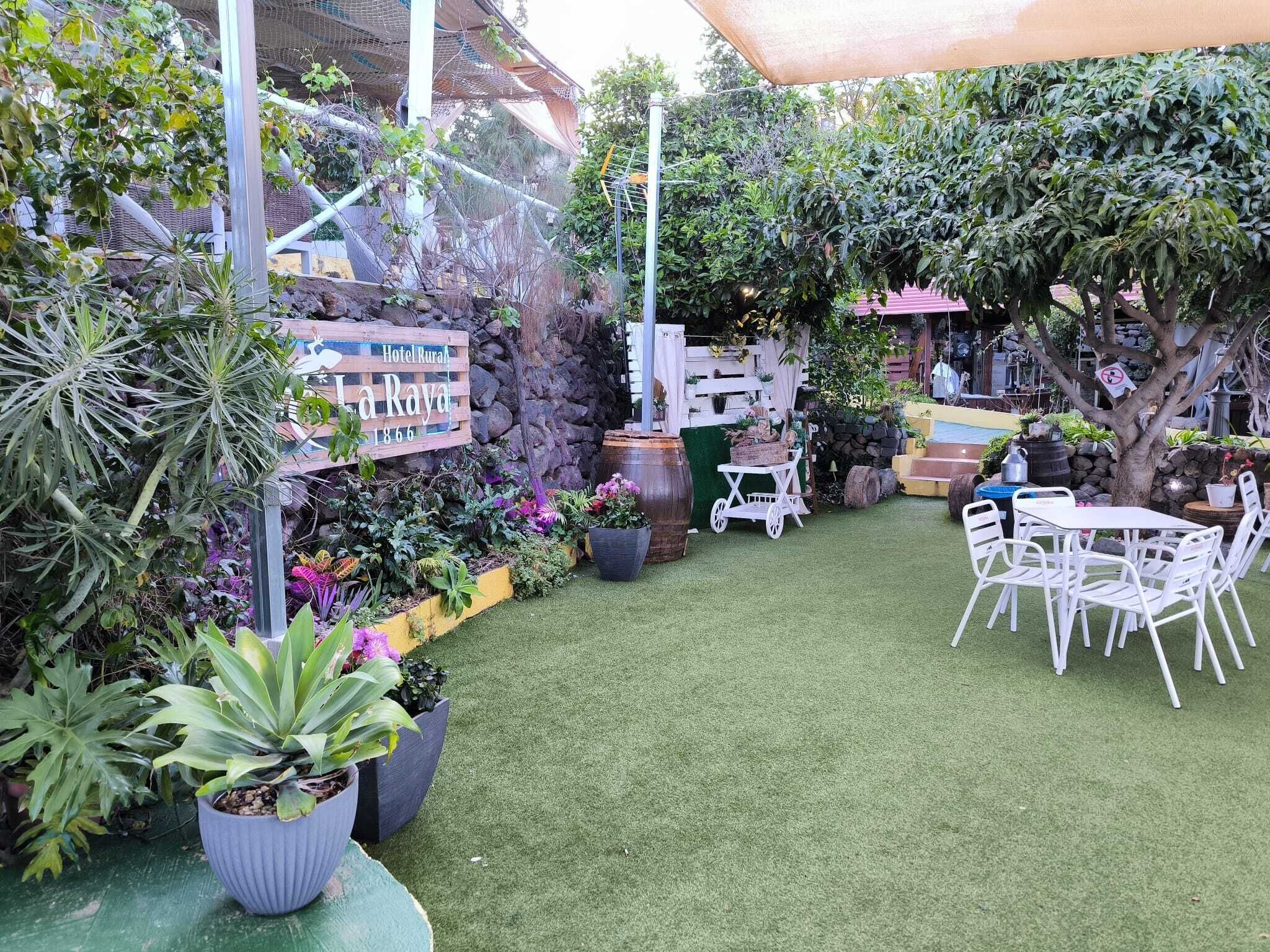 Un patio con césped artificial, plantas en macetas, un letrero de madera y mobiliario exterior.