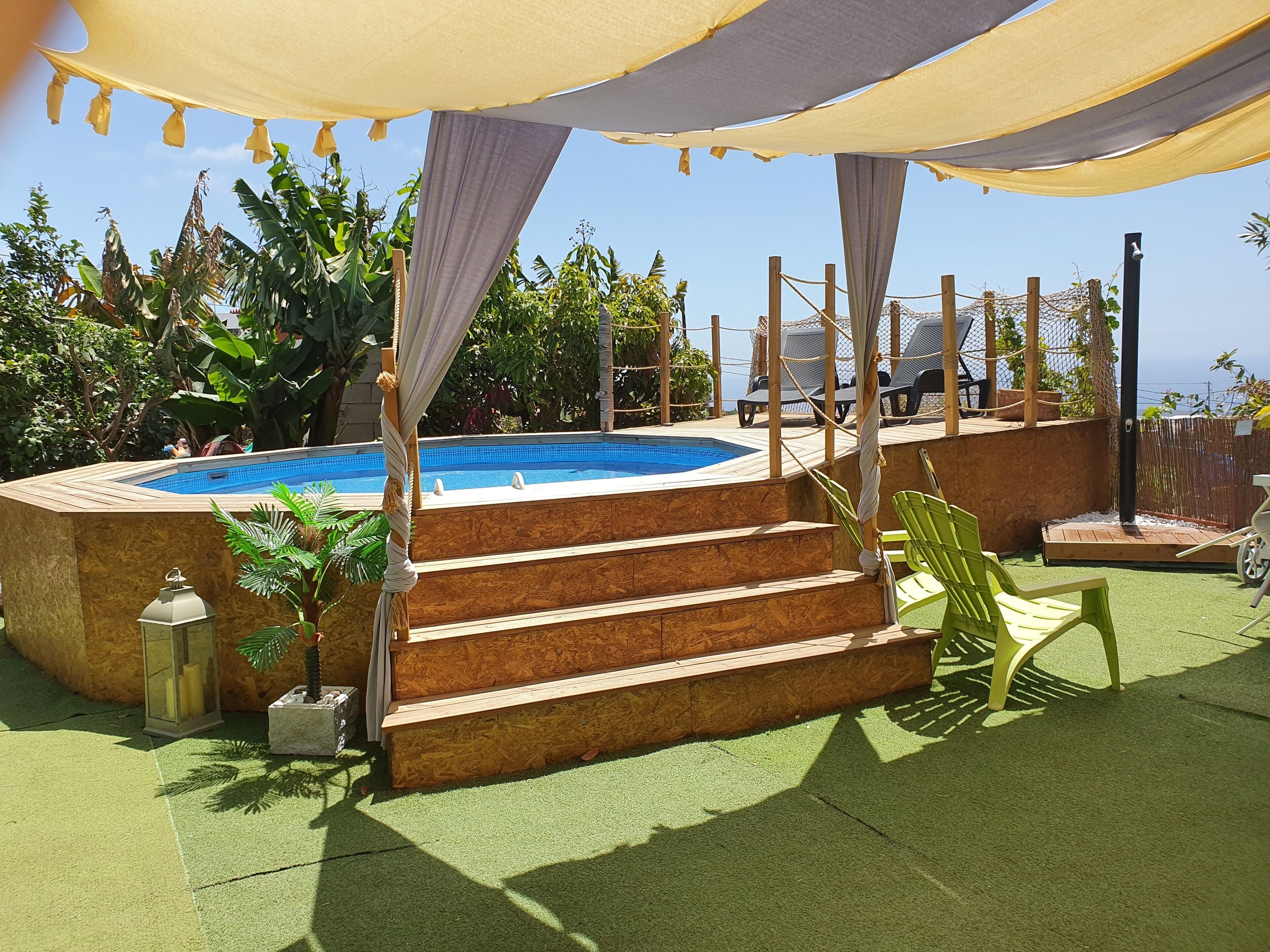 Zona de piscina con escalones que conducen a una terraza, rodeada de follaje y una cubierta.