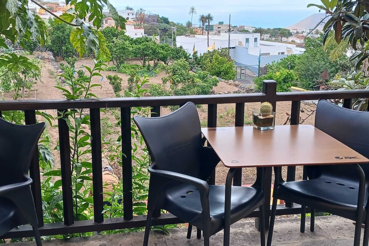 Un espace extérieur aménagé avec une table et des chaises, offrant une vue sur une colline verdoyante et des bâtiments situés au loin.