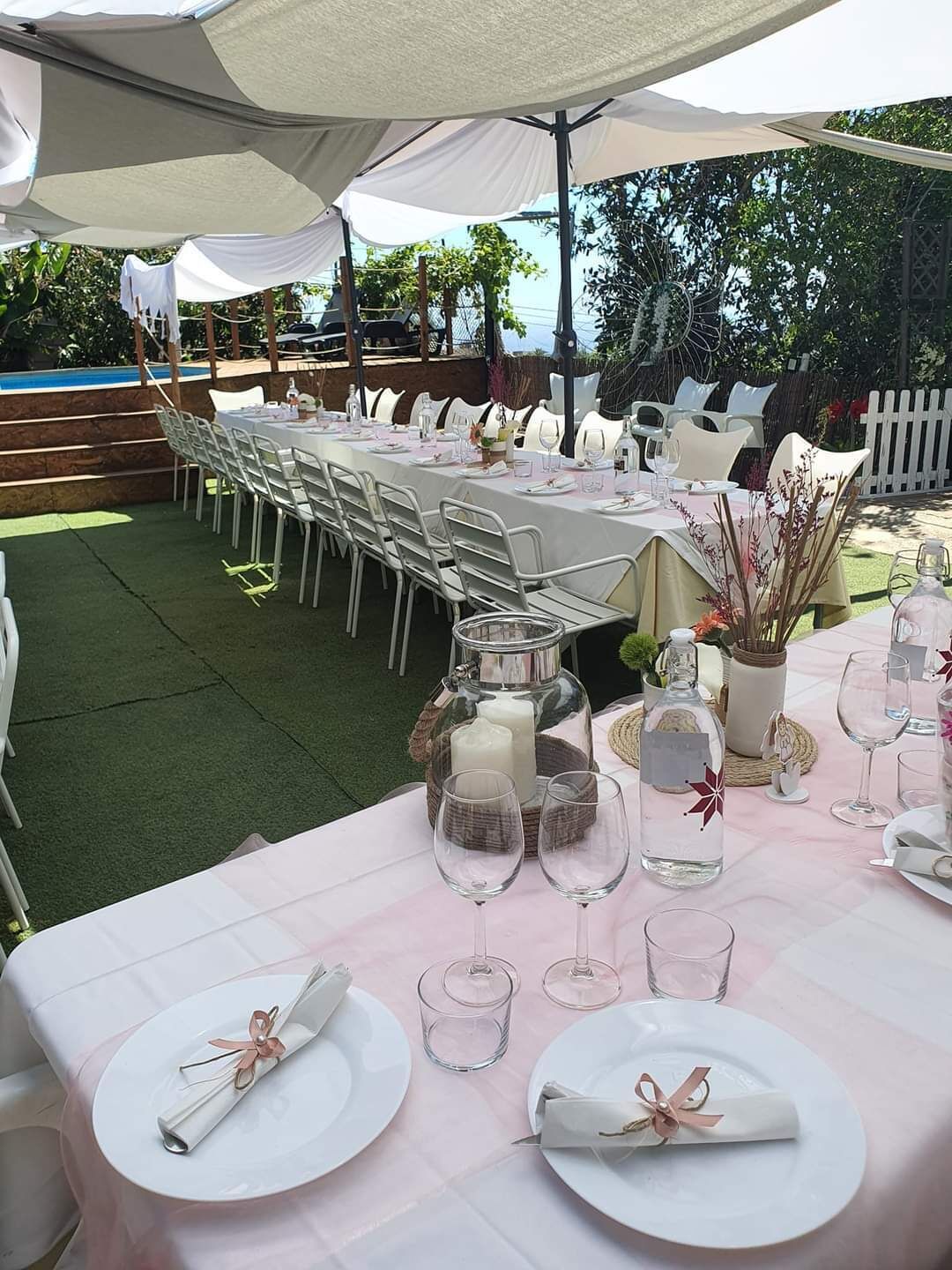 An outdoor dining area with white tables and chairs, a large umbrella, and a decorative centerpiece.