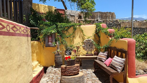 A courtyard with a stone floor, a wooden bench, a round table, and potted plants.