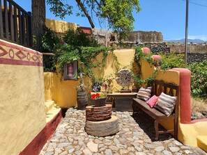 A courtyard with a stone floor, a wooden bench, a round table, and potted plants. - Hotel Rural La Raya 1866 (Güímar)