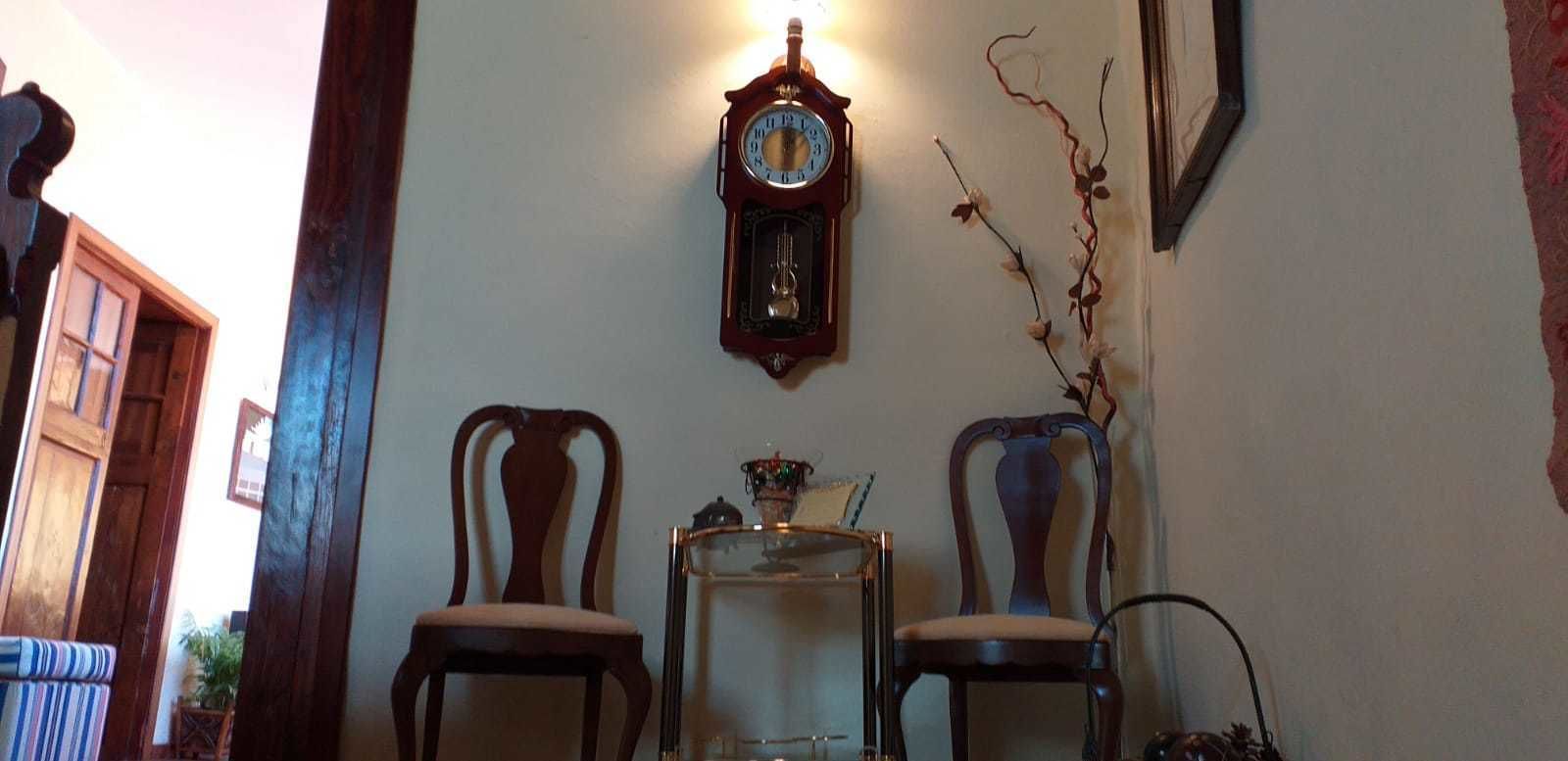 A room with two wooden chairs, a small table, and a wall-mounted clock.