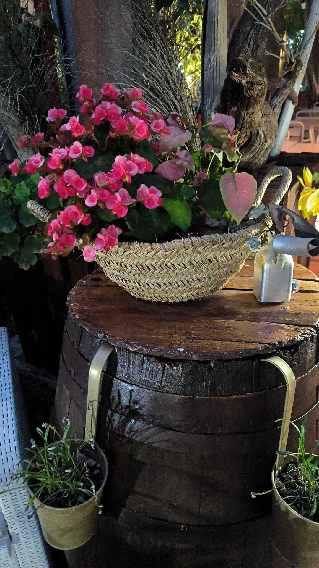 A rustic wooden barrel used as a planter with pink flowers and a woven basket.