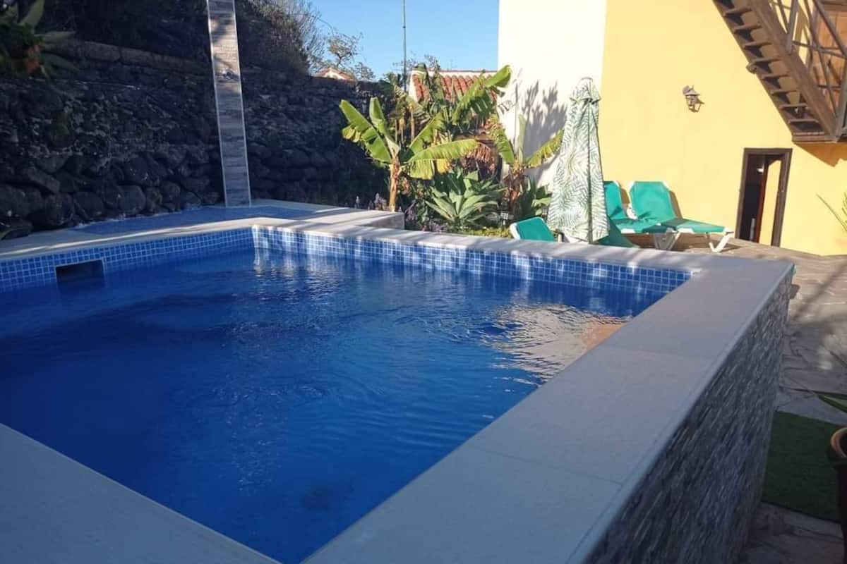 Une piscine bordée de pierres, entourée d’un mur jaune et d’un mur en pierre.