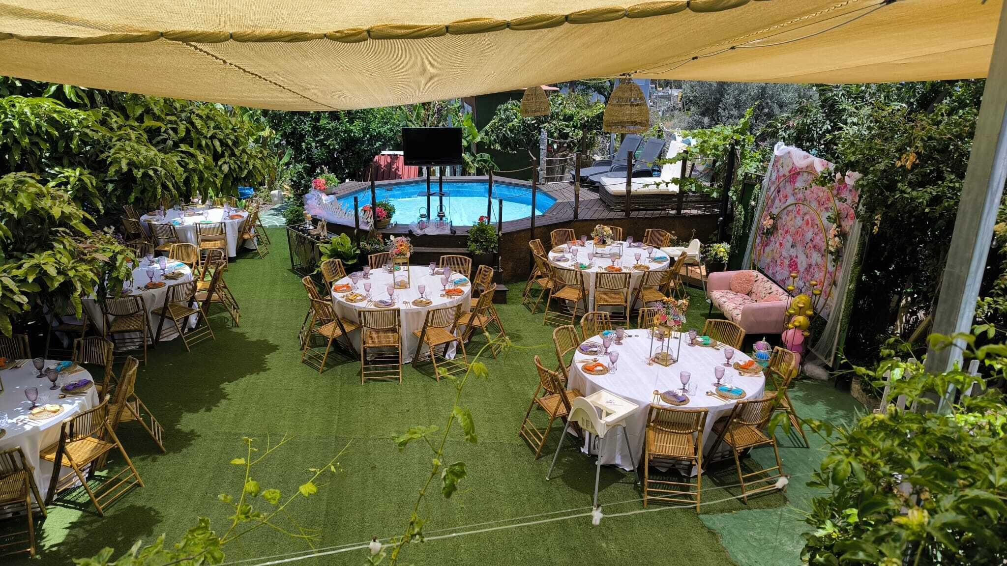 An outdoor dining area with round tables and chairs, a pool, and a covered seating area.