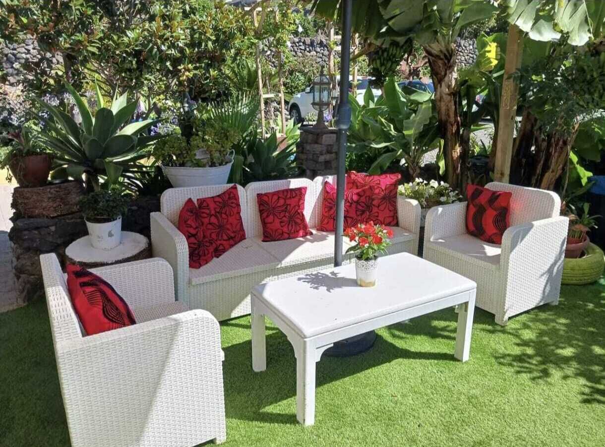 A patio area with white wicker furniture, including a sofa and two chairs, with red cushions. There is a white table in the center.