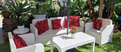 A patio area with white wicker furniture, including a sofa and two chairs, with red cushions. There is a white table in the center.
