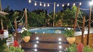 A poolside area with steps leading to the pool, surrounded by potted plants and string lights.
