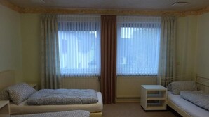 Une chambre avec deux lits simples, une petite table de chevet et une fenêtre avec des rideaux.