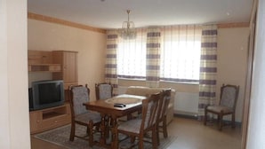 Un coin repas avec une table et des chaises en bois, un téléviseur posé sur un meuble, et une fenêtre agrémentée de rideaux à rayures.