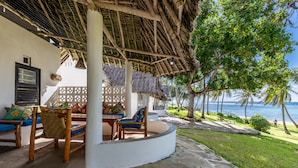 Un espace extérieur aménagé avec des meubles en bois et un toit de chaume, offrant une vue sur la plage et l’océan.
