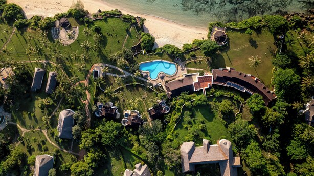 Vue aérienne d’un complexe hôtelier doté d’une piscine, d’une plage et d’une végétation luxuriante.