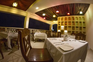 A restaurant with multiple tables, wooden chairs, and a decorative ceiling. - HillPark Amare Resort (Tiwi)