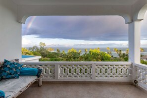 A balcony with a white railing, a wooden bench, and a view of the ocean and palm trees. - HillPark Amare Resort (Tiwi)