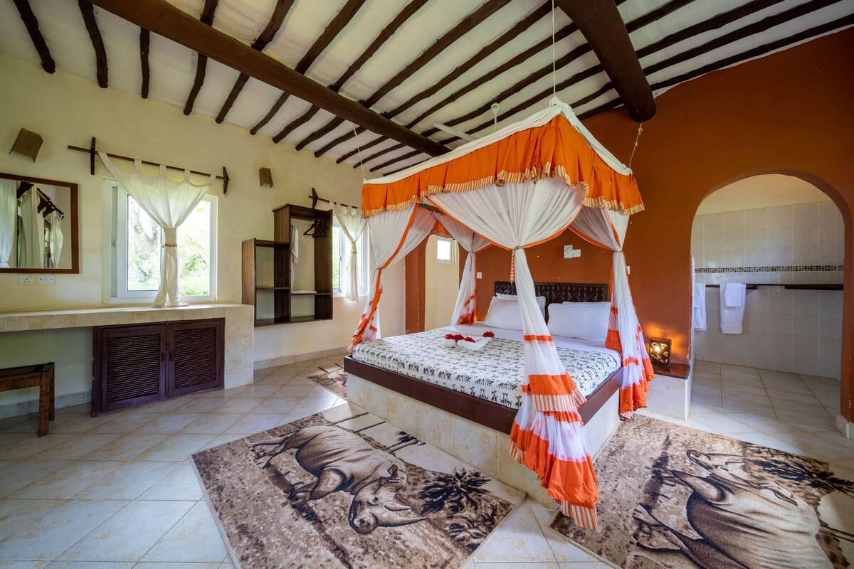 Une chambre à coucher avec un lit à baldaquin, un banc, un miroir et une fenêtre avec des rideaux.