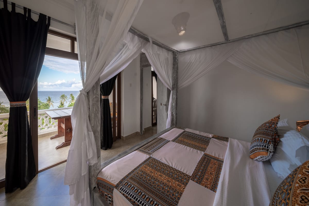 Une chambre à coucher avec un lit, des rideaux blancs et une vue sur l’océan.