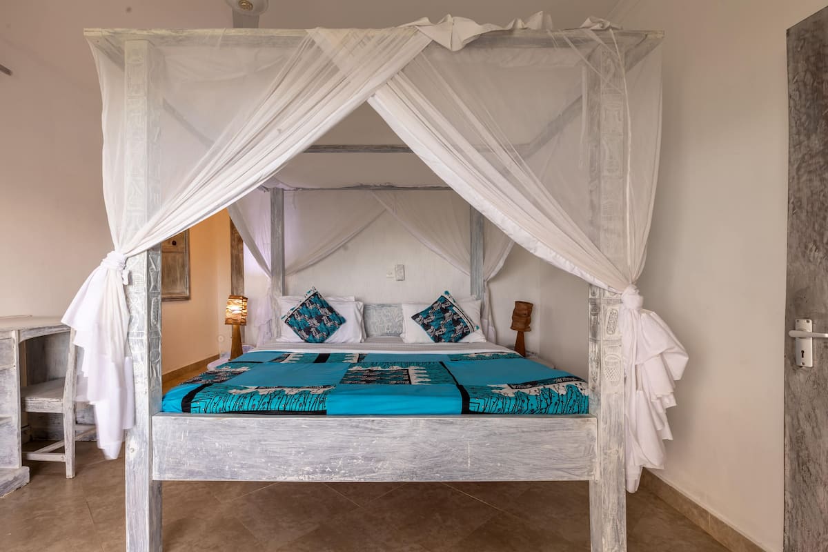 Un lit à baldaquin à quatre poteaux, avec un couvre-lit blanc et des touches de bleu, une table de chevet en bois et une lampe fixée au mur.