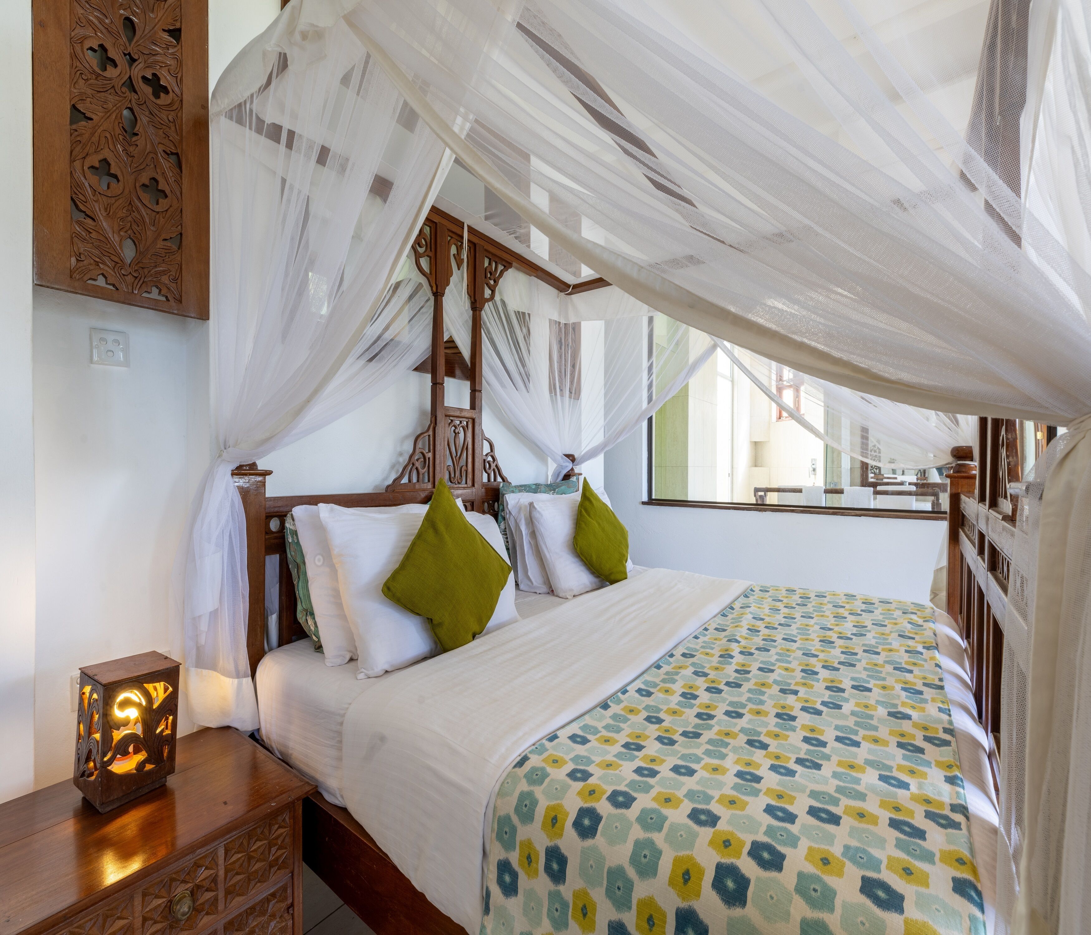 A bed with a canopy, a bedside table with a lamp, and a patterned bedspread.
