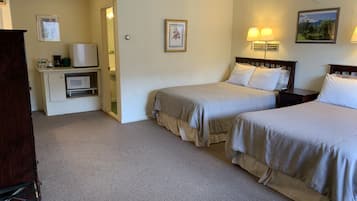 Quarto de hotel com duas camas, uma cozinha compacta, banheiro e uma pequena escrivaninha.